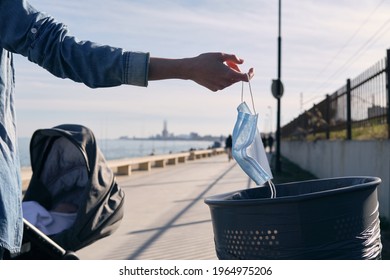 Woman With Baby Carriage Throwing Her Mask In The Trash On A Promenade, End Of Pandemic Thanks To Covid-19 Vaccine, Post-pandemic, Freedom, Virus-free Holiday, Virus-free Summer