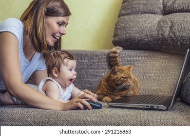 The Woman With A Baby And A Cat At The Laptop Lying On The Couch