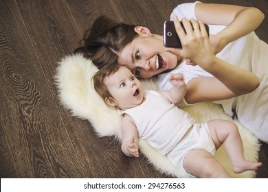 Woman with a baby doing a selfie lying on wooden floor - Powered by Shutterstock