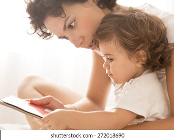 Woman And Baby Girl Reading. Mother And Her Little Baby Girl On Bed.