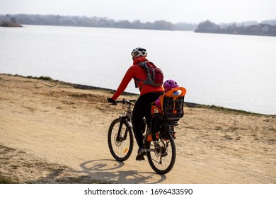 Woman With Baby On Bike Rides On Sandy Shore Near Water
