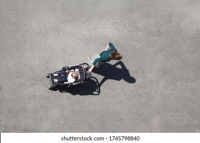 Woman With A Baby Stroller Standing On A City Street, Top View. Concept Of Motherhood, Single Mom With Pram