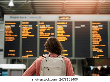 Woman, back and airport with flight schedule on board with information display for global immigration. Person, backpack and international travel with digital time table on screen, location or arrival