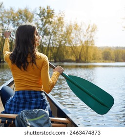 Woman, back and canoeing in nature on lake, wellness hobby and backpack for supplies with paddle for rowing. Vacation, relax and explore exercise on travel holiday, canoe boat and trees on river bank