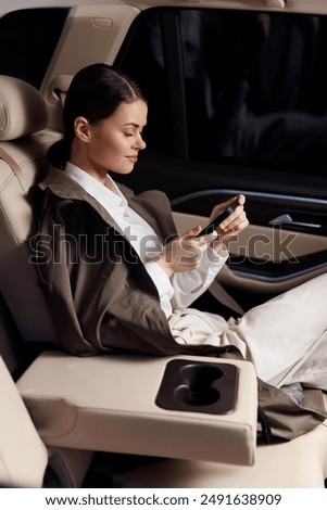 A woman in the back seat of a car holds a cell phone, attentively looking at its screen, showcasing a modern lifestyle moment during a car ride