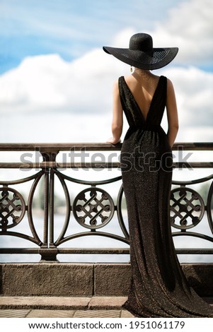 Woman Back Side View in Hat and Evening Dress Outdoor. Fashion Model Rear View looking away. Luxury Lady in long Gown at Promenade looking at Sky