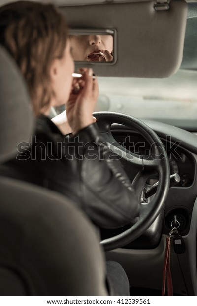 Woman back view driving a car, coloring lips\
with lipstick