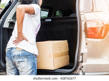 Woman With Backache While Lifting Box In The Car.