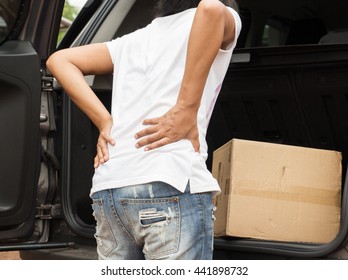 Woman With Backache While Lifting Box In The Car.