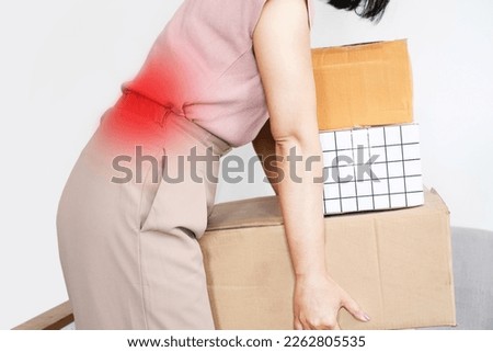woman with a backache while lifting boxes, back pain caused by wrong movement or bad posture 