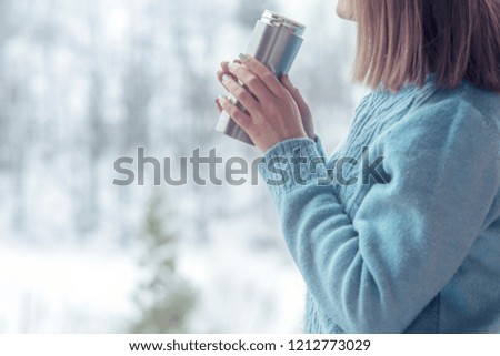 Woman in the background of a winter forest in a thermos bottle in hands
