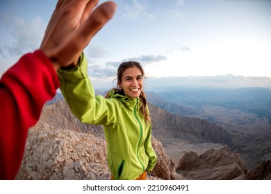 A woman with a backpack climbed to the top of the mountain and gives a high five, hiking in the mountains, success in achieving the goal
 - Powered by Shutterstock