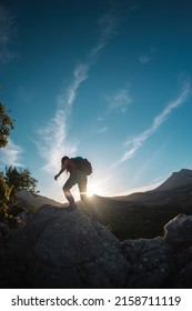 A woman with a backpack climbs to the top, hiking in the mountains, success in achieving the goal, the silhouette of a girl against the backdrop of a mountain at sunset - Shutterstock ID 2158711119