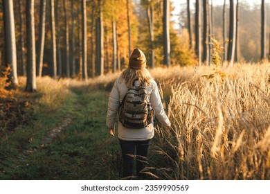 Woman with backpack hiking in autumn forest. Hiker walking on footpath in woodland. Golden sunrise in fall season morning - Powered by Shutterstock