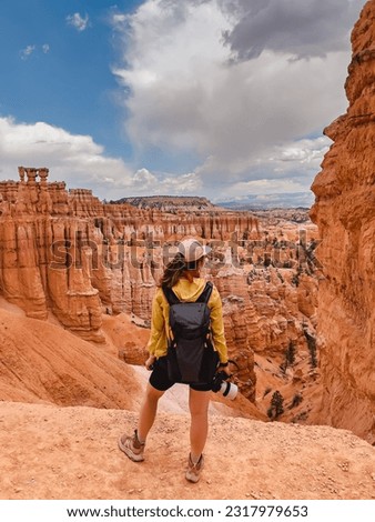 Woman with a backpack holding a photo camera looking on the rock formations in Bryce canyon national park, view from the back