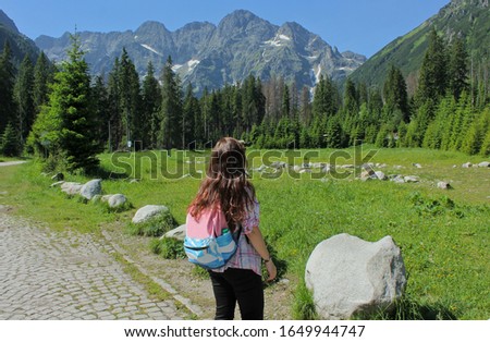 Woman with backpack looks at mountains. Back view. Girl traveles the Tatra National Park in the Rybi Potok (the Fish Brook) Valley, Zakopane, Poland.