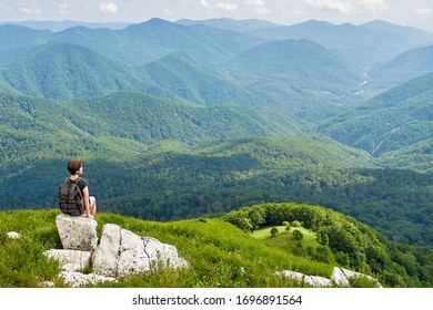 Woman with backpack sitting on top of the mountain. View of the green meadow. Mountain tourism and a sense of freedom.