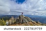 Woman with backpack standing on massive rock formation at Steinerne Hochzeit, Saualpe, Lavanttal Alps, border Styria Carinthia, Austria, Europe. Panorama of alpine meadows and snowcapped mountains