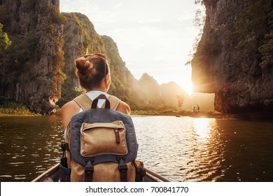 Woman With Backpack Swims On Boat Among Karst Mountains To Meet Her Friends. Tam Coc,  North Of Vietnam.
Travel And Active Lifestyle, Summer Holiday Concept.