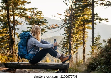 Woman with backpack and thermos resting on bench in forest. Relaxation during hiking in mountain - Shutterstock ID 2200678739