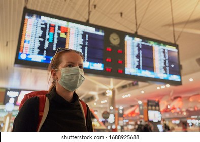 A Woman With A Backpack Wearing An Anti-virus Mask On Her Face At The Airport Arrivals Board                             