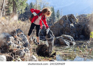 Woman Backpacker Ecologist Picking Up Trash and garbage in nature Environment of a Beautiful Mountain Lake - Powered by Shutterstock