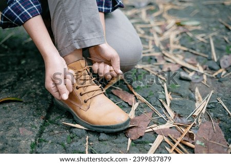 A woman backpacker laces up her right shoe while crouching down.