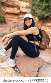Woman backpacker smiling at the camera while taking a break on a rock during a hike through the canyons of grand canyon national park, enjoying the wilderness and outdoor adventure