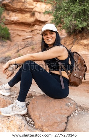 Woman backpacker smiling at the camera while taking a break on a rock during a hike through the canyons of grand canyon national park, enjoying the wilderness and outdoor adventure