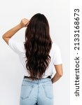 Woman from backside on white background. Female with curly hair. Rear view of brown-haired young lady with long hair, wearing white t-shirt over white background, isolated 