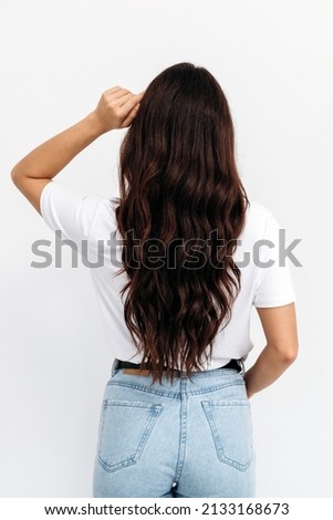 Woman from backside on white background. Female with curly hair. Rear view of brown-haired young lady with long hair, wearing white t-shirt over white background, isolated 
