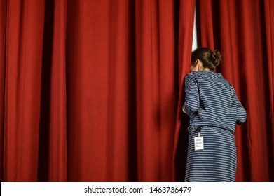 woman with a backstage pass looking behind the red curtains on a stage