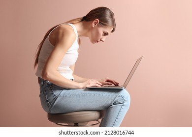 Woman with bad posture using laptop while sitting on stool against pale pink background - Shutterstock ID 2128016744