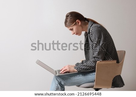 Woman with bad posture using laptop while sitting on chair against light grey background, space for text