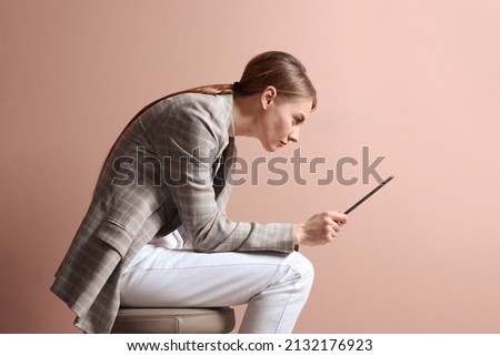 Woman with bad posture using tablet while sitting on stool against pale pink background