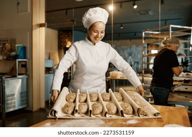 Woman baker preparing sweet buns pastries with sesame seeds - Powered by Shutterstock