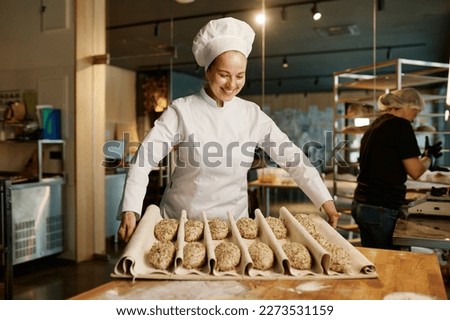 Woman baker preparing sweet buns pastries with sesame seeds