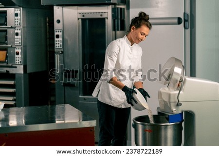 Woman baker putting dough into kitchen planetary mixer for mixing to prepare delicious bread
