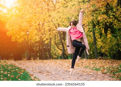 Woman ballerina in pointe shoes in golden autumn park, standing in beautiful pose on yellow leaves