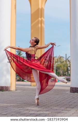 Woman ballerina in red ballet dress dancing in pointe shoes next to the old columns. Ballerina standing in beautiful ballet pose