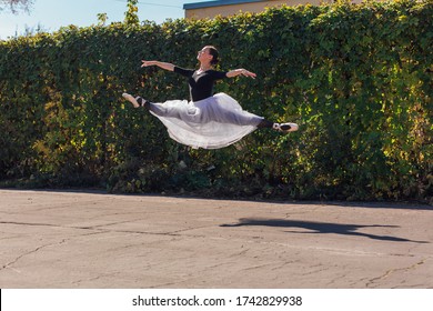 Woman ballerina in a white ballet skirt dancing in pointe shoes in a golden autumn park. Ballerina jumping doing a split - Powered by Shutterstock