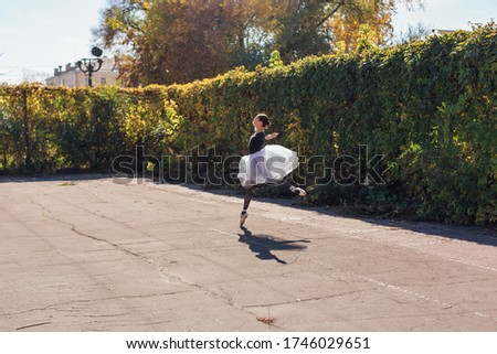 Woman ballerina in a white ballet skirt dancing in pointe shoes in a golden autumn park. Ballerina jumping doing a split