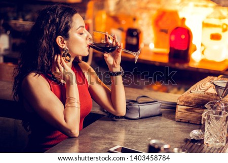 Woman in bar. Woman in red dress sitting at the bar counter and drinking red wine alone