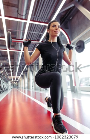 woman with barbell flexing muscles and making lunge in gym