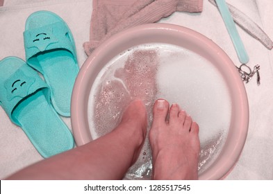 Woman bare feet in soap water bath relaxing after active walk.Painful banion in female foot.Above view on wash and pedicure girl legs