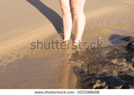 Woman with bare feet in water on the sandy beach
