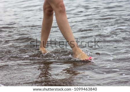 Woman bare foot walking on the summer beach. Walking along wave of sea water and sand on the beach, close-up.