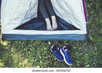 Woman barefoot in a tent on green camping field.