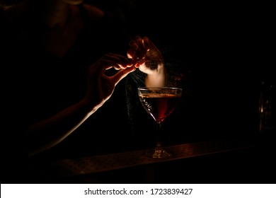 Woman Bartender Accurate Sprinkles Juice From Citrus On Beautiful Illuminated Glass With Red Wine On Dark Bar.