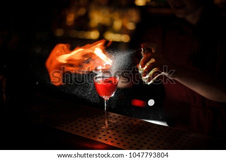 Woman bartender sprinkling a cocktail glass filled with tasty Aperol syringe summer cocktail with a peated whisky and making a smoky note